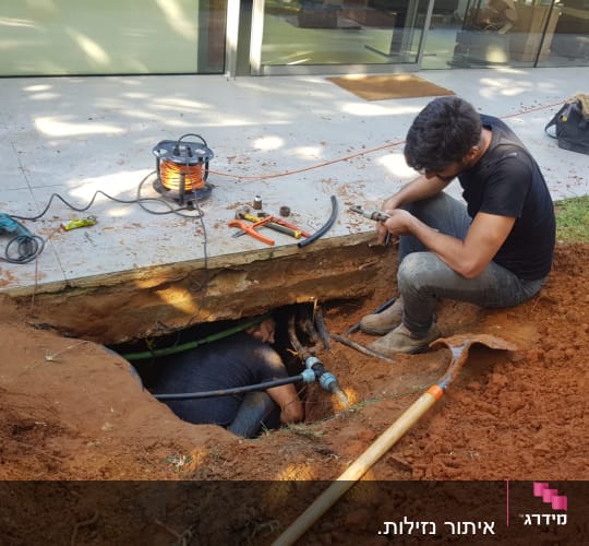 עובד מתקן צינור מים בחפירה עם כלים
